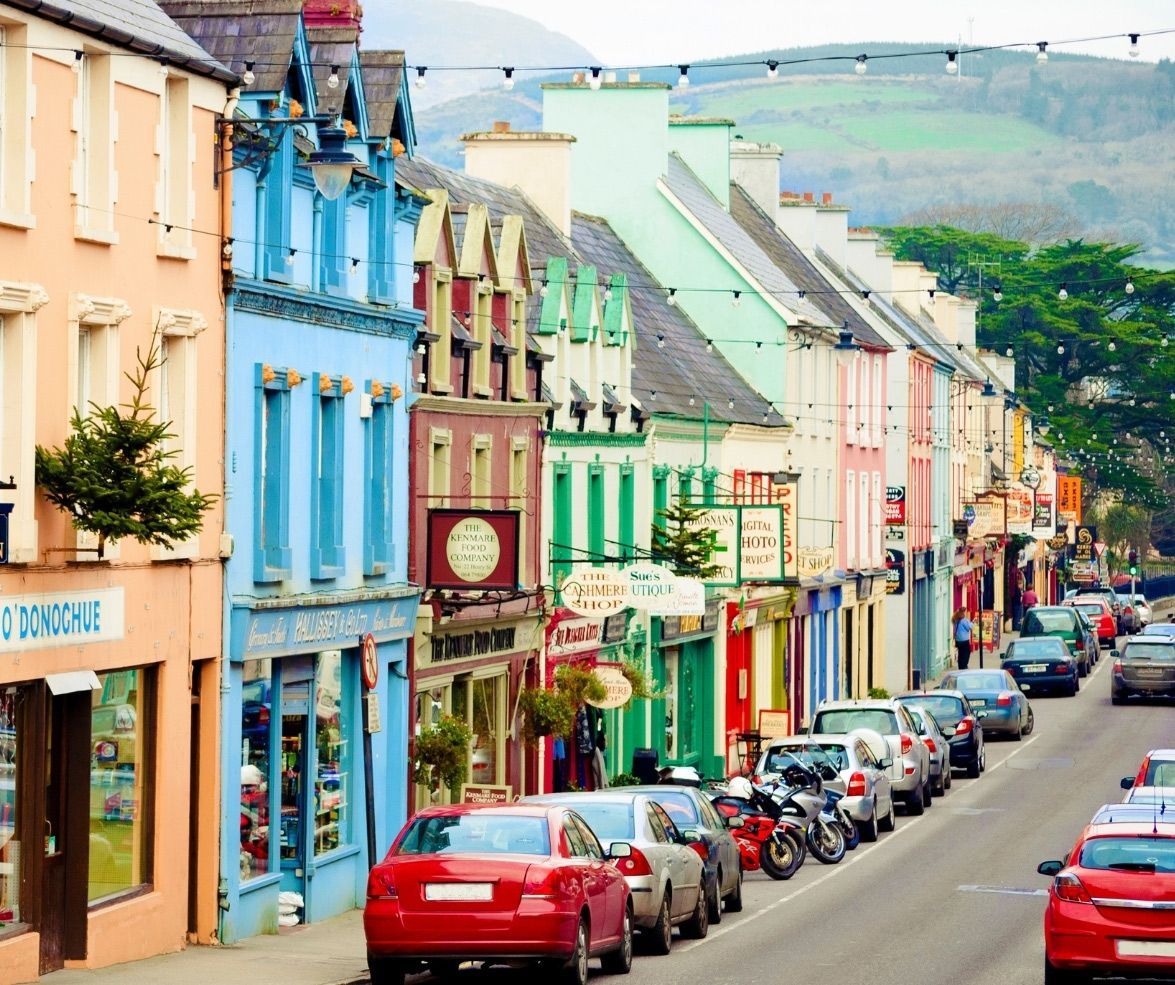 Colorful buildings line a street in a town, cars parked along the road