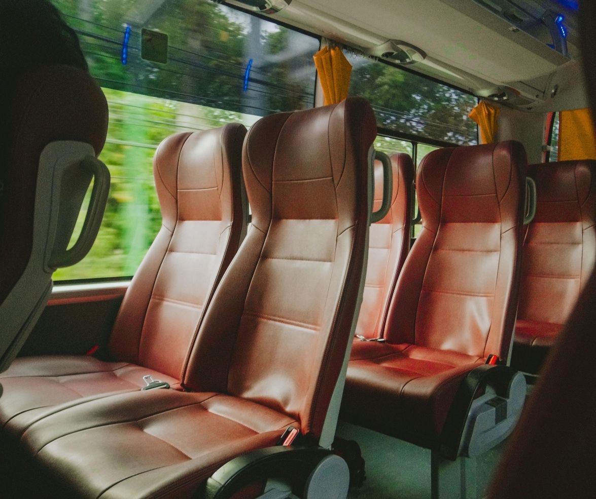 Empty bus seats with brown leather upholstery line a brightly lit interior