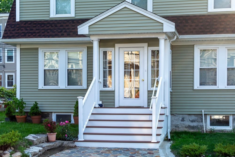 A sage green house exterior featuring a front entrance with a gabled portico, white stairs, and white window frames.
