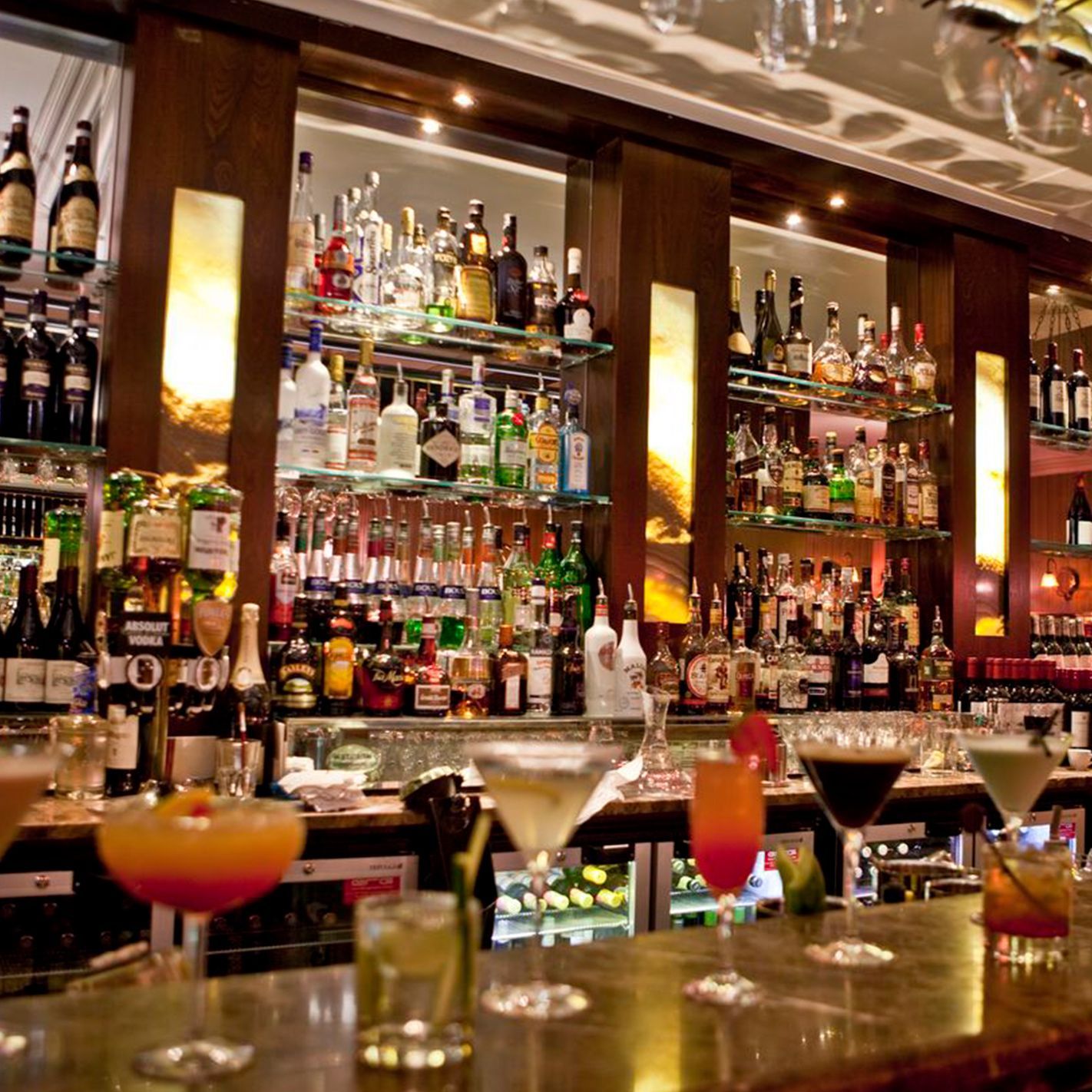 Bar with a wide selection of liquor bottles. Several cocktails sit on the counter.