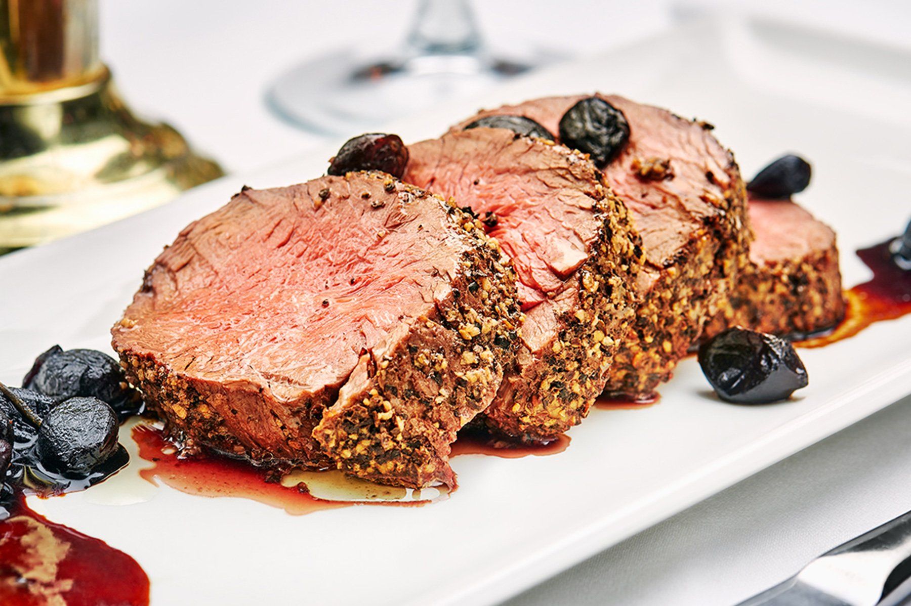 Sliced, seared beef tenderloin on white plate with dark olives and sauce.