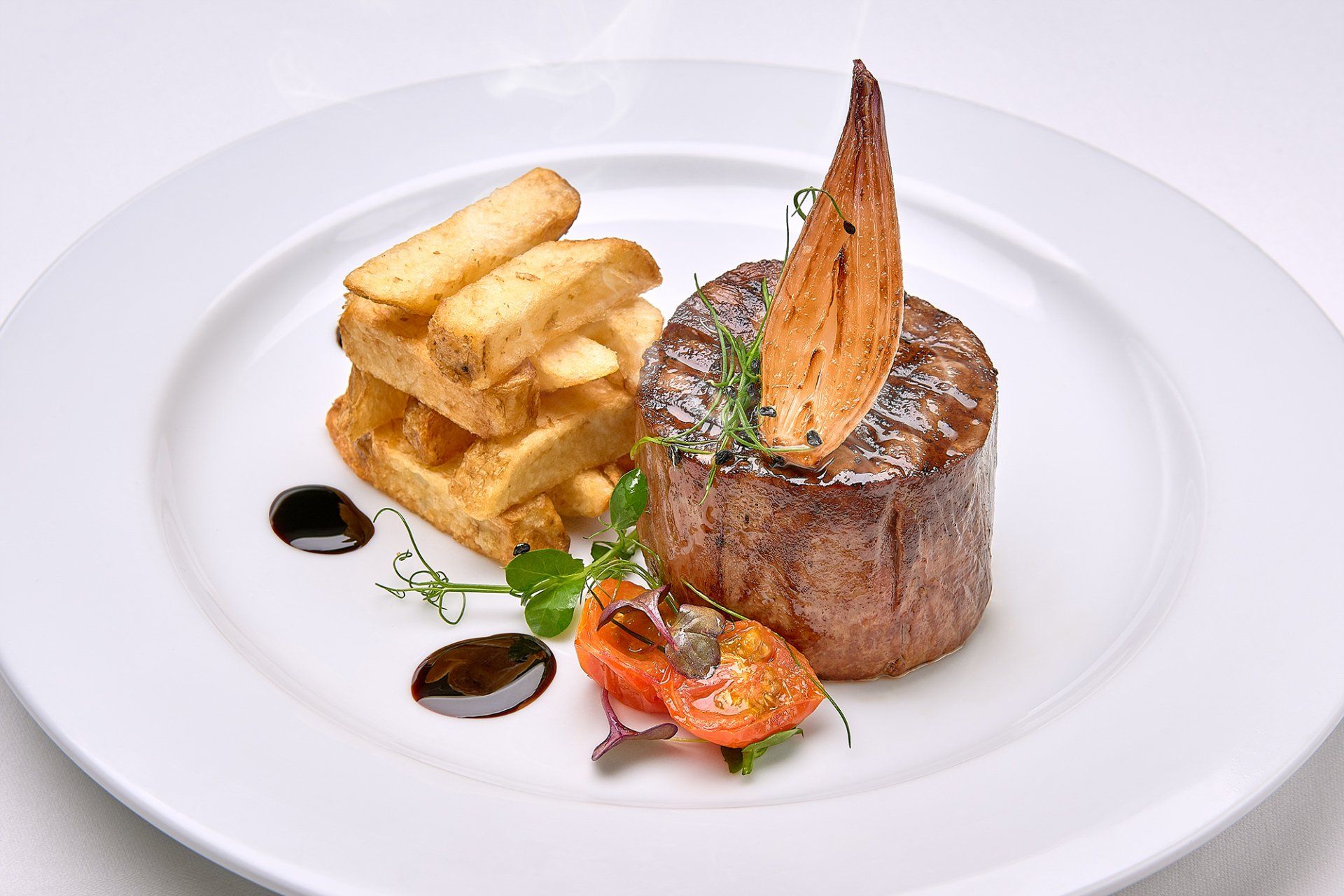 Steak with chips and garnish on a white plate.