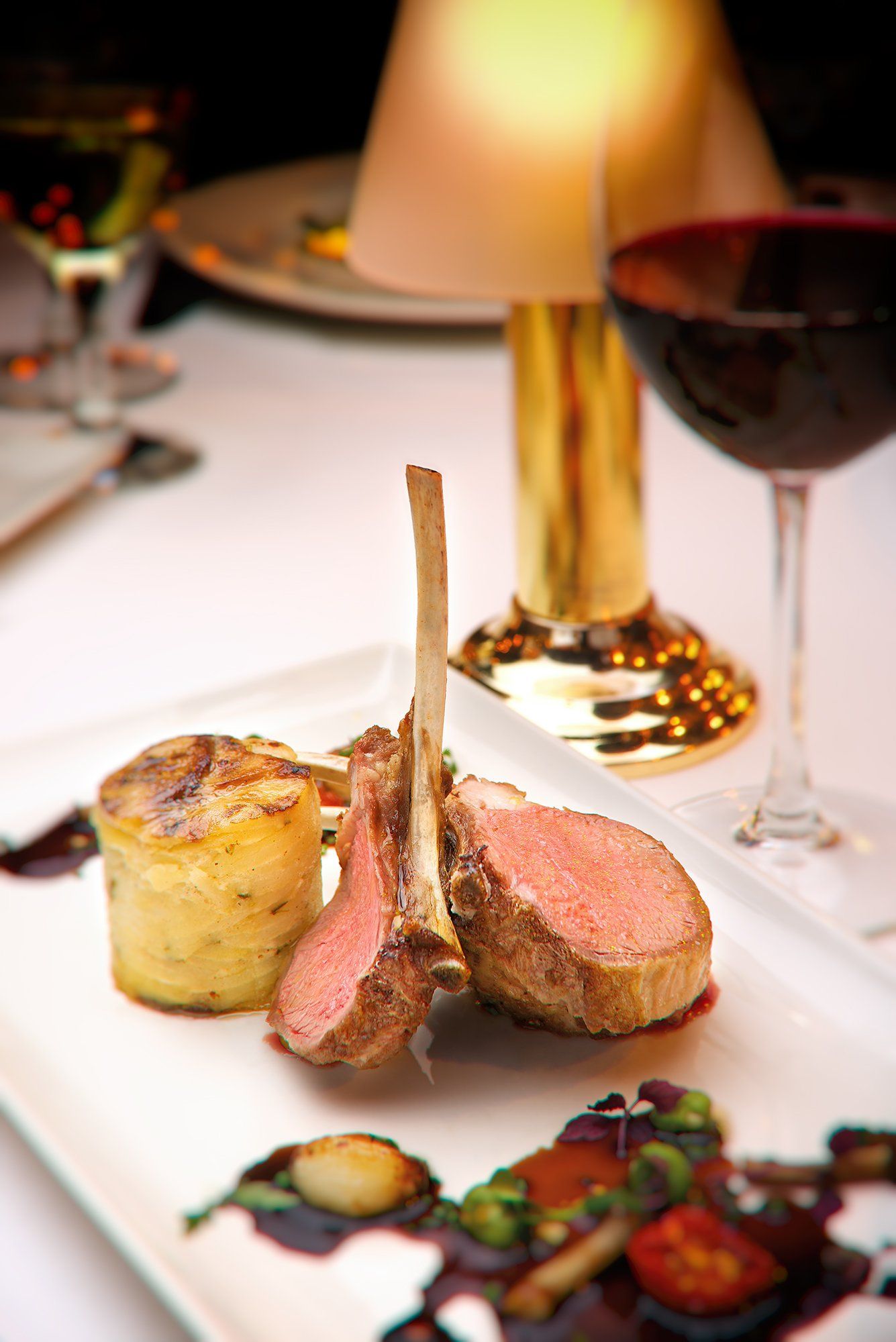 Rack of lamb with potatoes and red wine on a white plate in a restaurant.