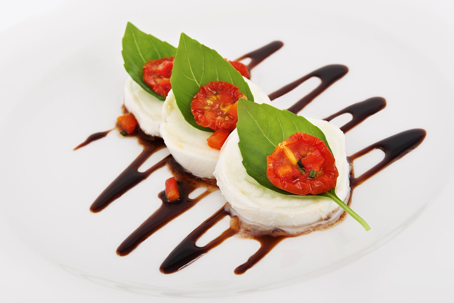 Caprese salad: mozzarella, tomato, basil, and balsamic glaze on a white plate.
