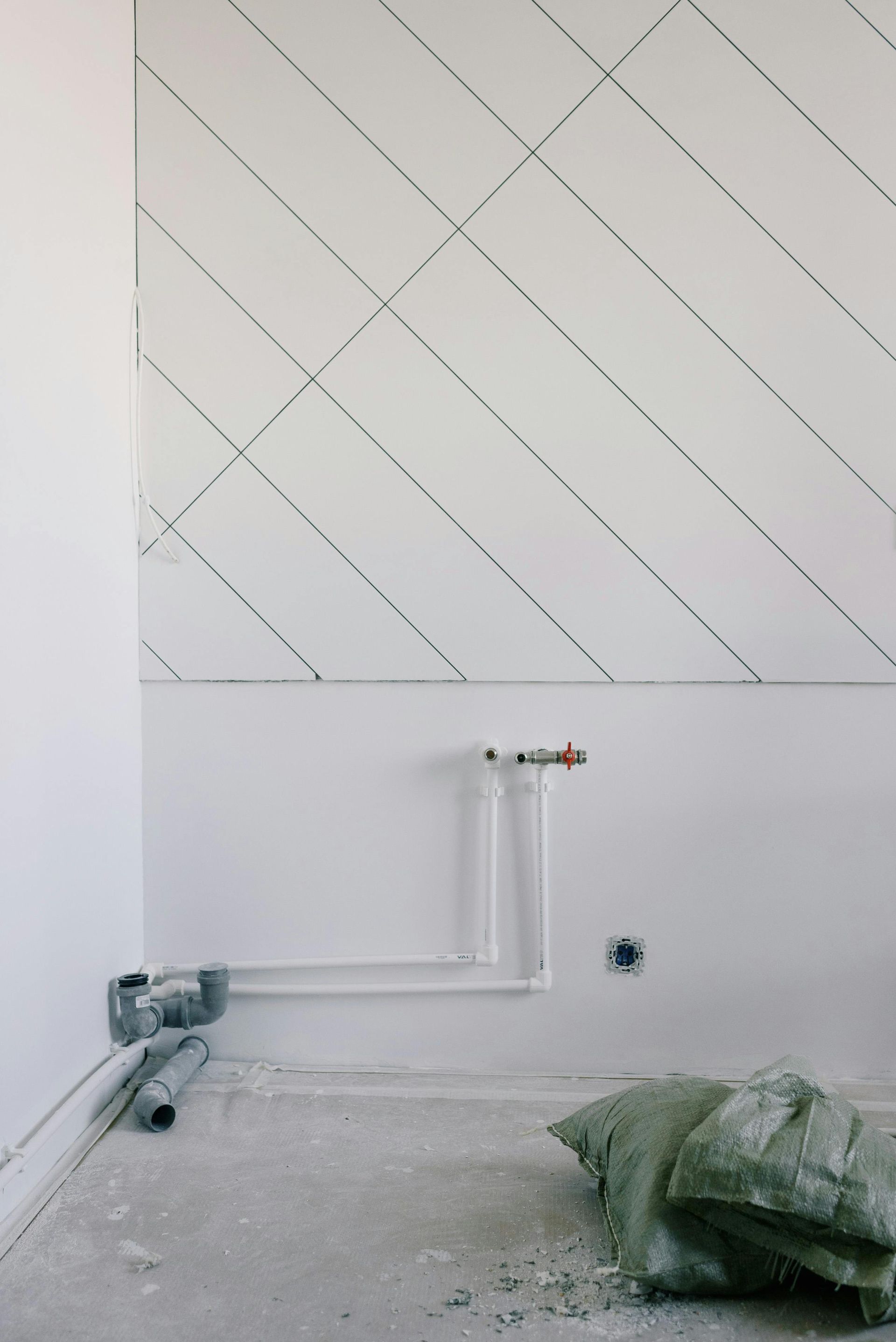 White wall with diagonal lines and exposed plumbing during construction.