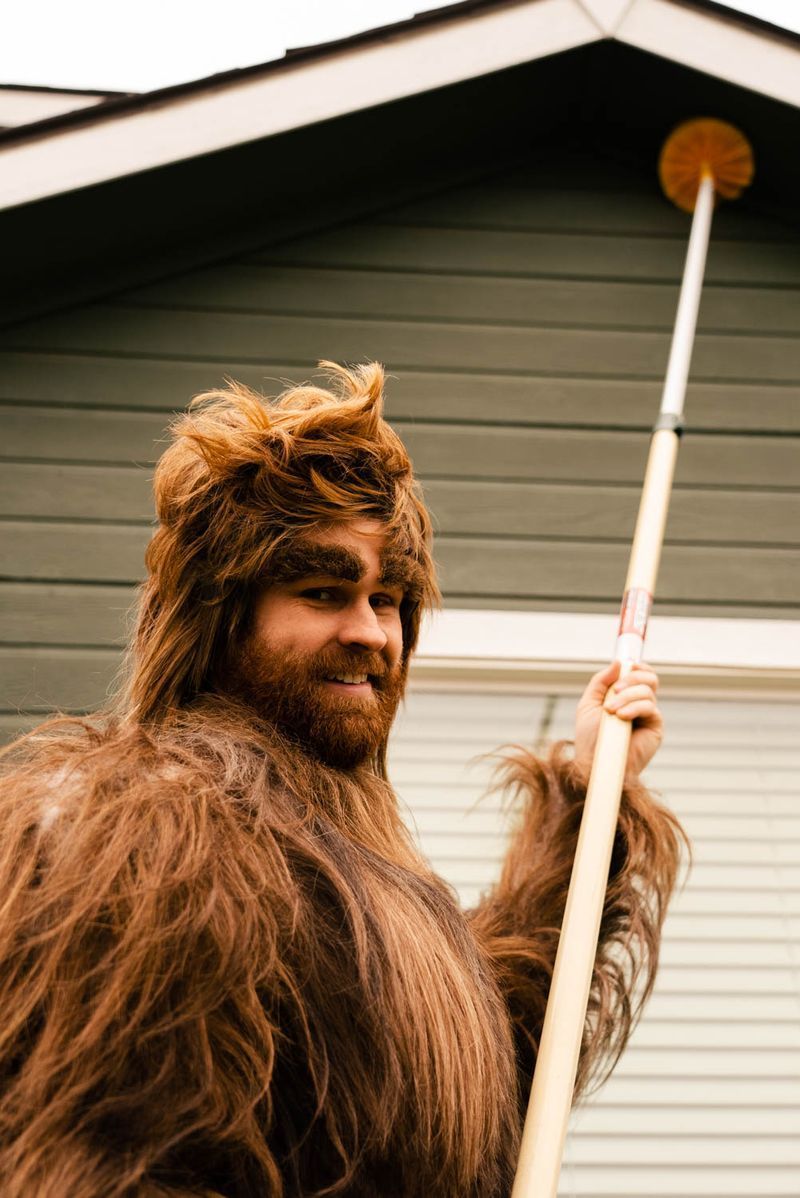 A man dressed as a bigfoot is holding a pole in front of a house.