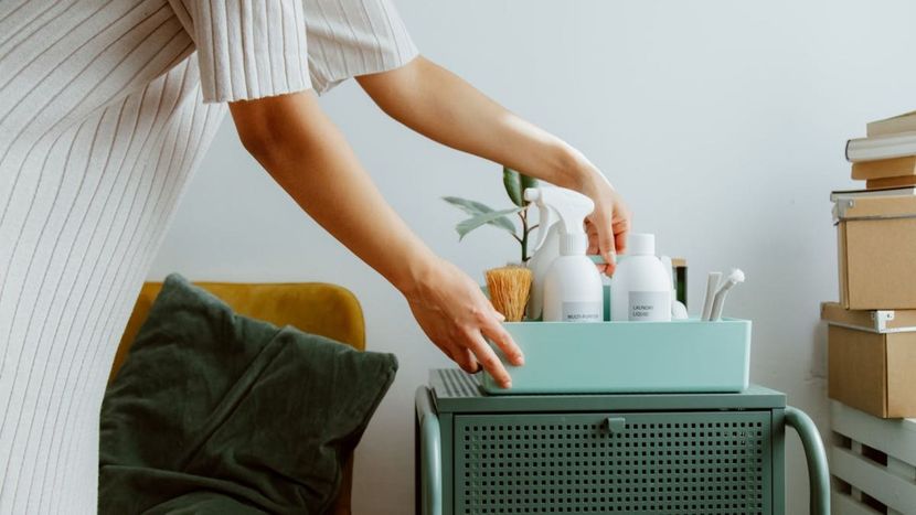 Una mujer está colocando una caja de productos de limpieza en una cómoda.