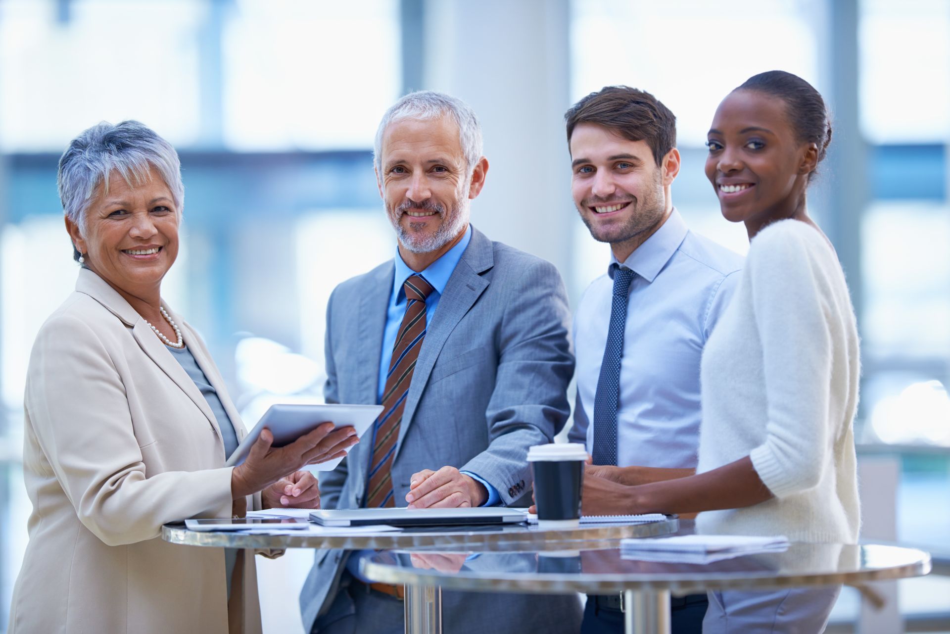 Business team, diverse ages, smiling, discussing at a table, bright office setting.