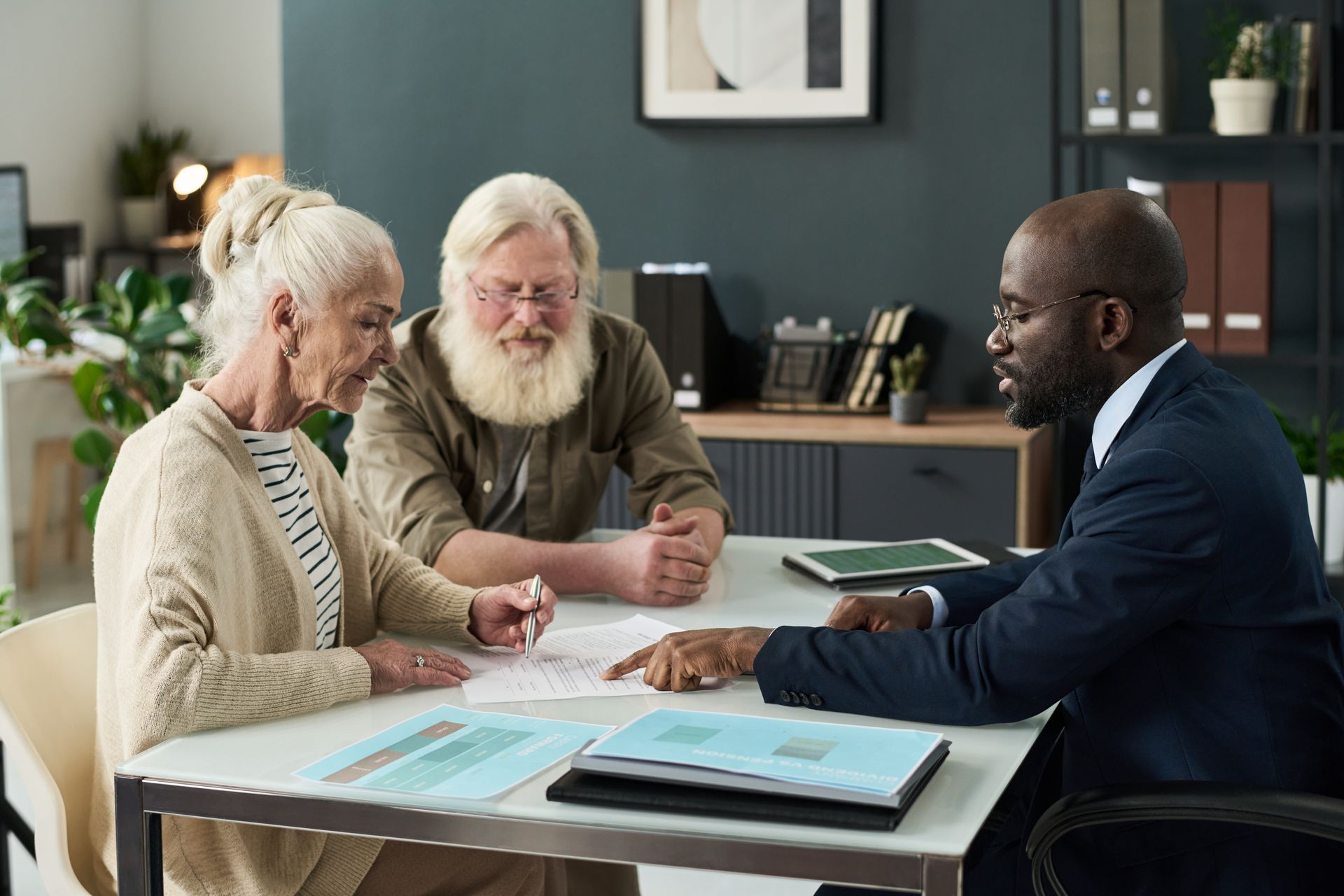 Older couple reviewing documents with a financial advisor at a desk.
