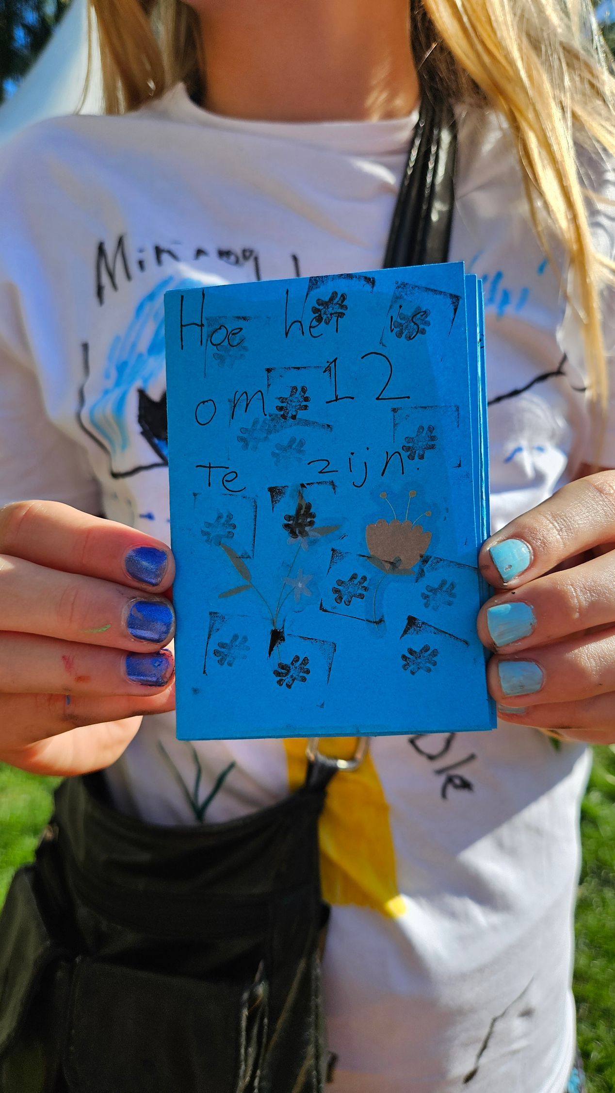 Een persoon houdt een blauw rechthoekig voorwerp vast met zwarte bloemmotieven. De handen zijn blauw gelakt.