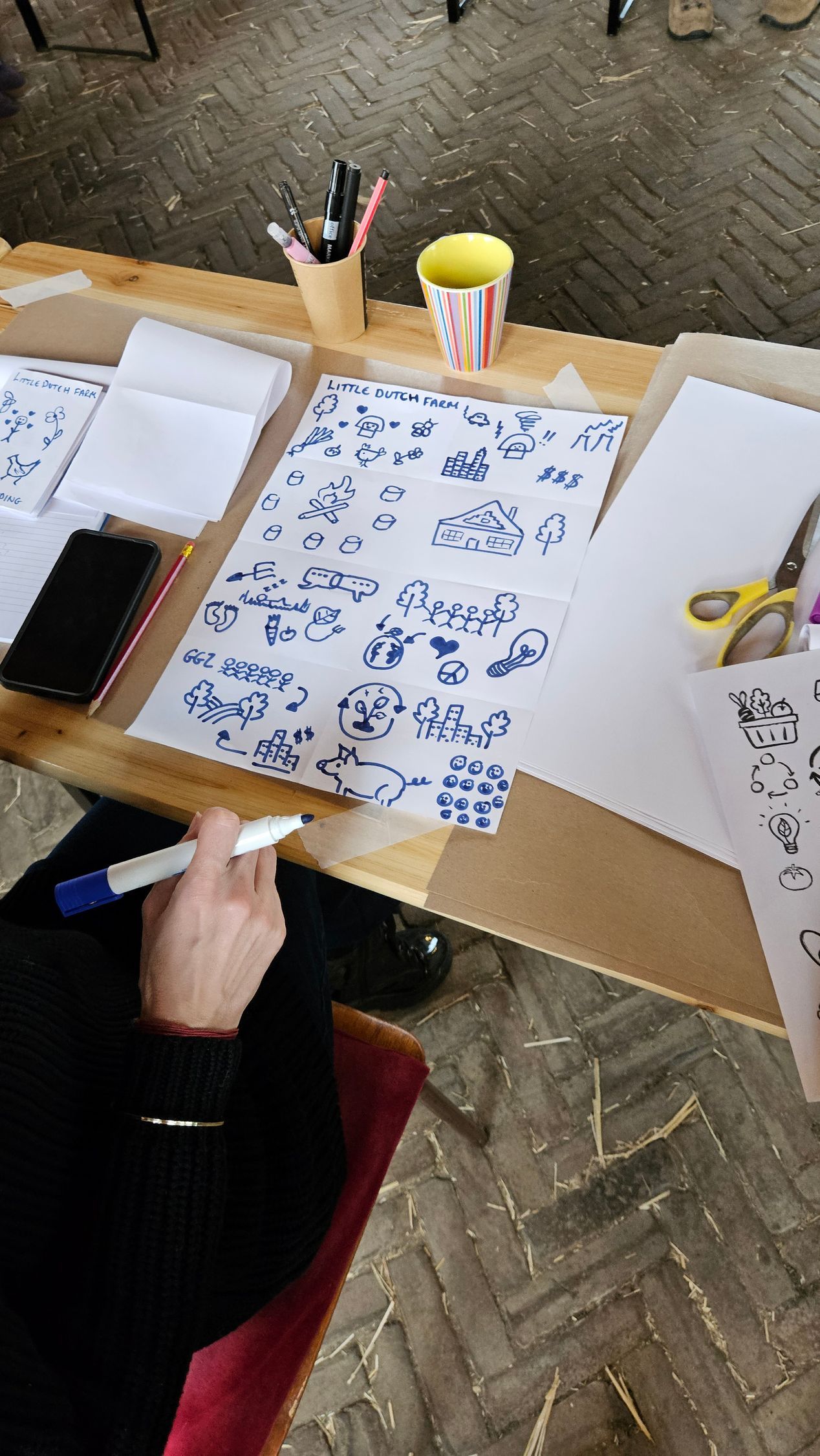 Iemand tekent blauwe patronen op papier aan een tafel met teken- en schildersbenodigdheden.