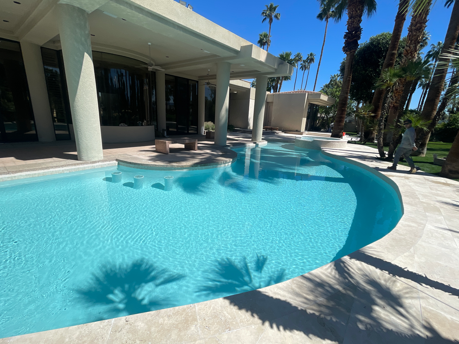 A large swimming pool in front of a house with palm trees