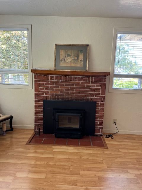 A living room with a red brick fireplace centered between two windows. A wood-burning stove sits inside the fireplace.