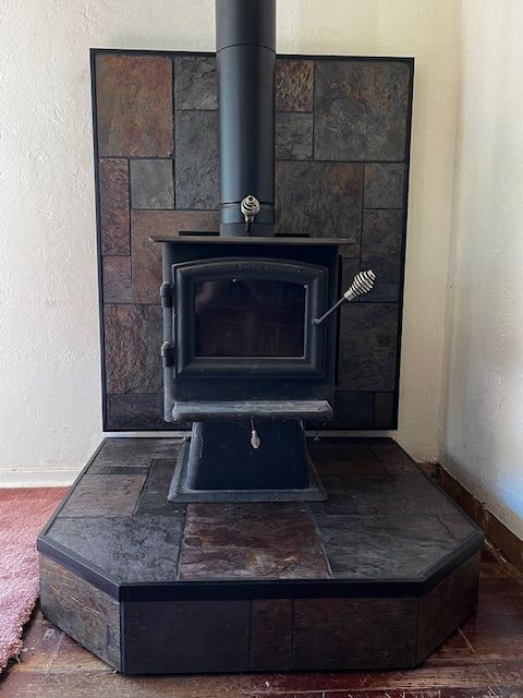 A black wood-burning stove with a matching flue pipe, set against a slate tile backsplash and hearth.