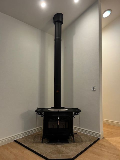 Black wood-burning stove in a corner, with a tall chimney. Tile base and white walls.