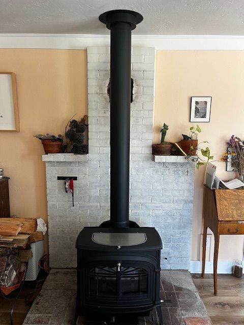 A black wood-burning stove with black chimney against a white brick facade, flanked by peach walls.