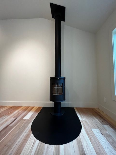 Black wood-burning stove with chimney on a black floor plate in a room with wooden floors and white walls.