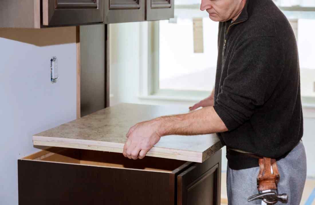 Man removing  a countertop in a kitchen; he's holding the countertop over the cabinet.