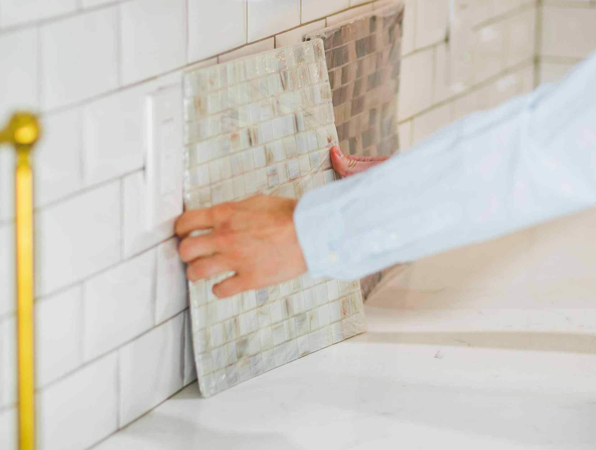 Person holding a tile sheet against a white subway tile backsplash.