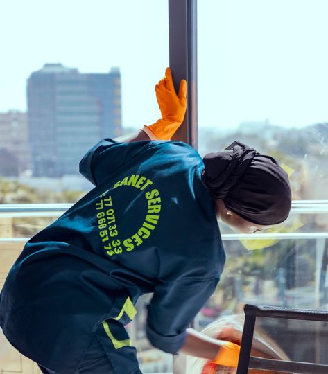 Une femme portant un tablier et des gants jaunes sourit avec les bras croisés.