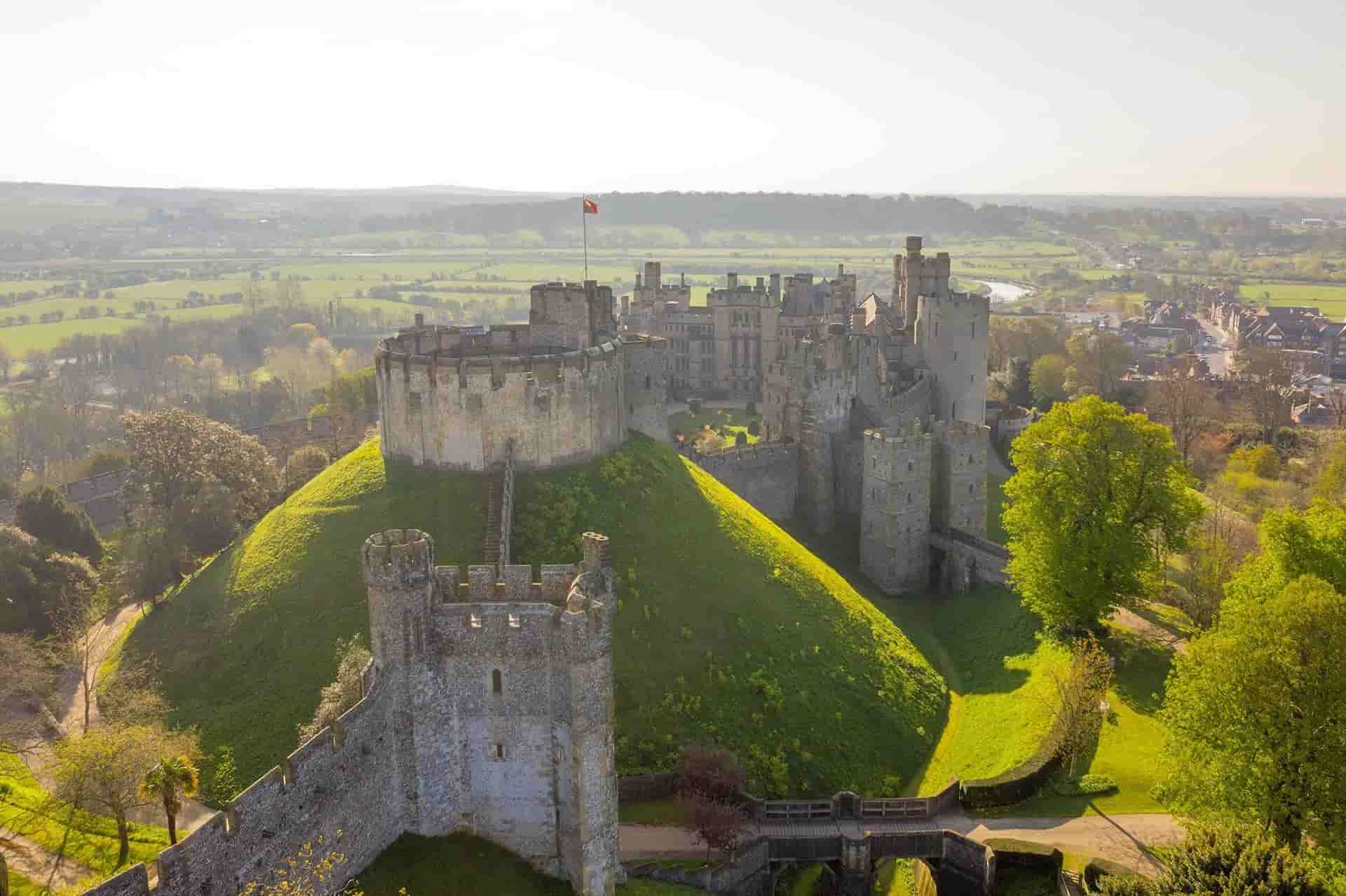 An aerial view of a castle on top of a hill surrounded by trees and grass.