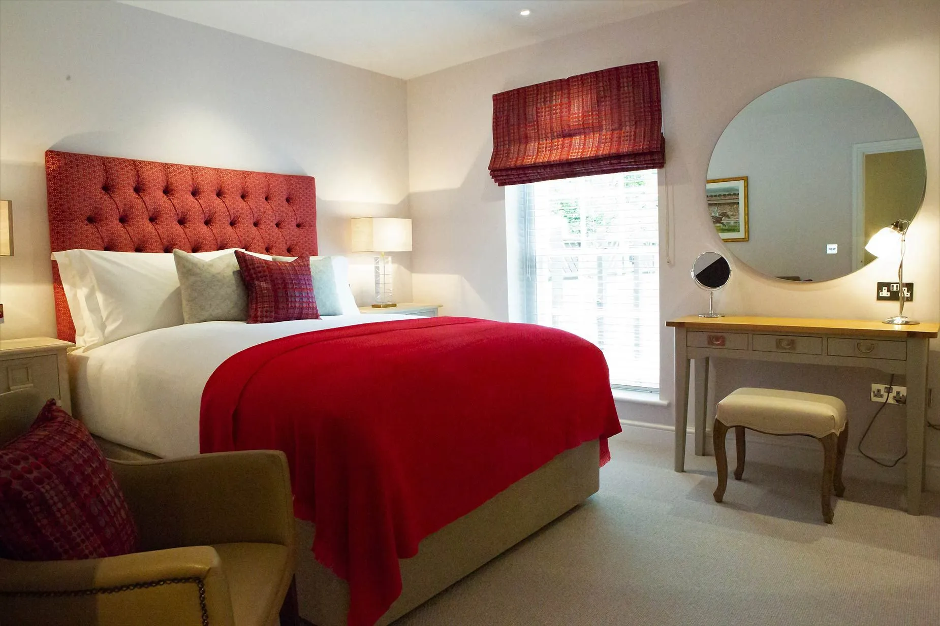 A bedroom with a bed , chair , dresser and mirror.