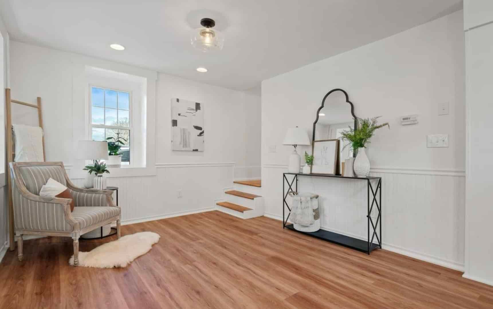 A living room with hardwood floors , a chair and a mirror.
