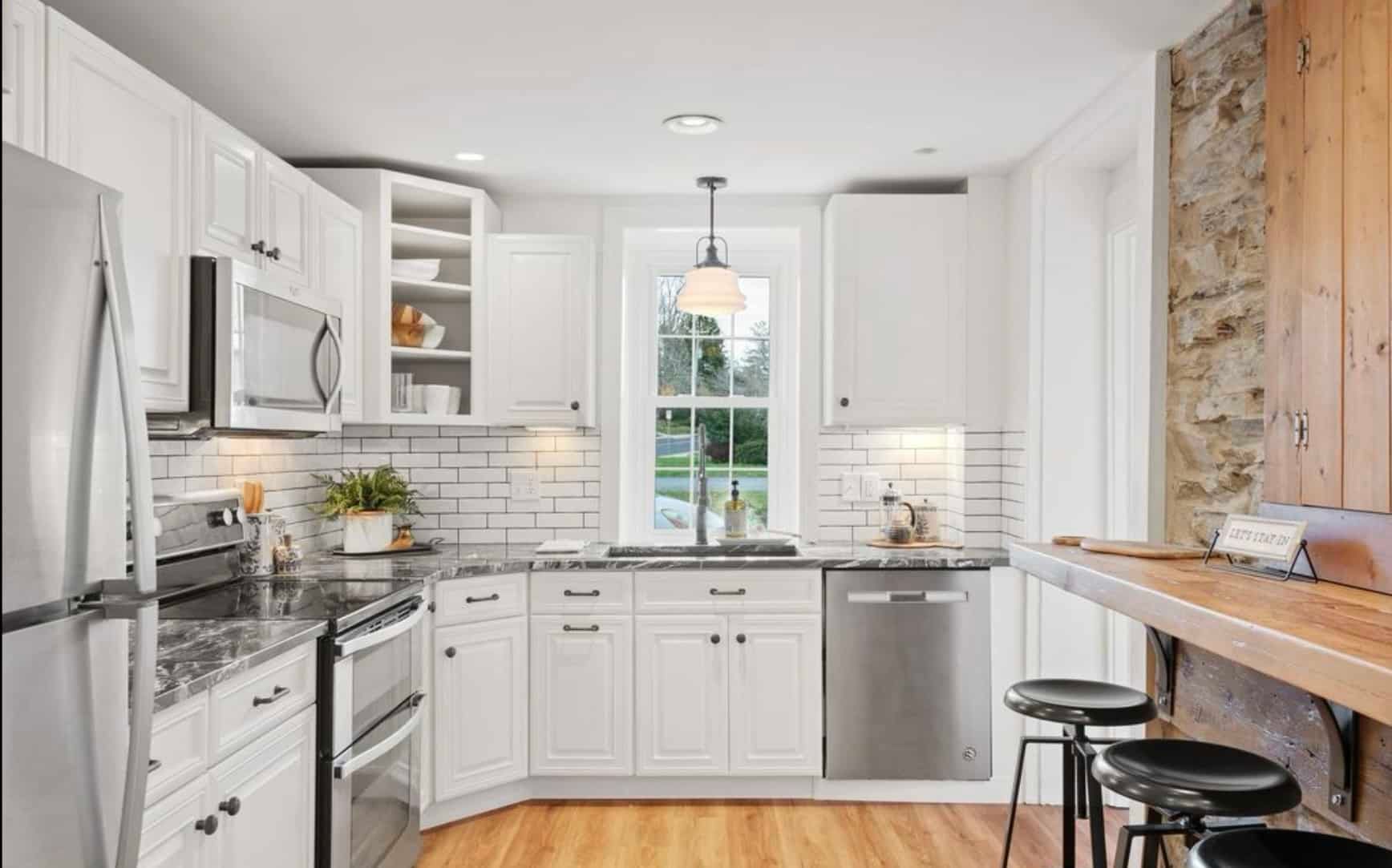 A kitchen with white cabinets , stainless steel appliances , granite counter tops and a window.