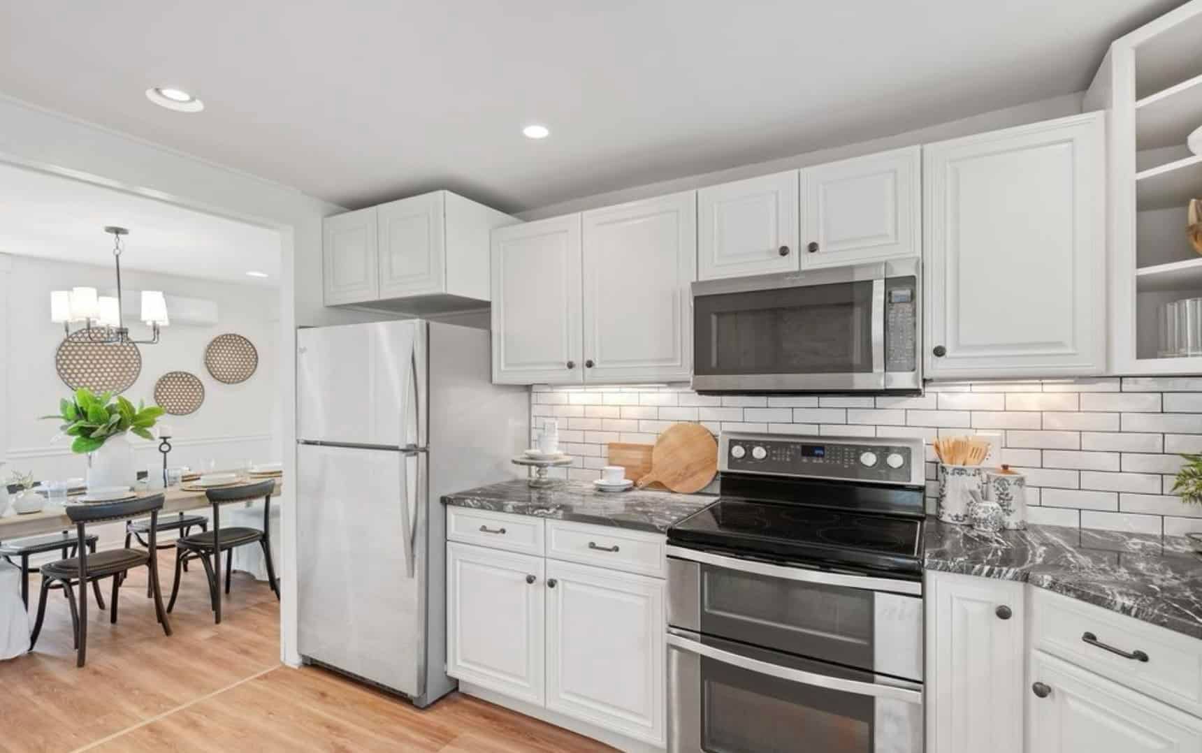 A kitchen with white cabinets , stainless steel appliances , a refrigerator , microwave , and stove.