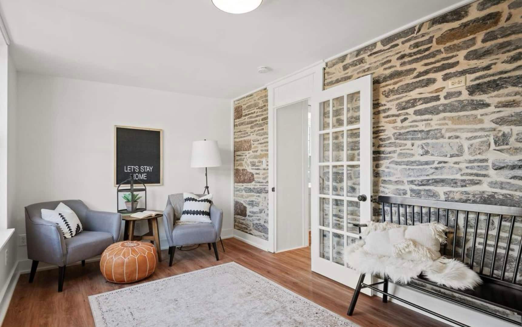A living room with a stone wall , two chairs , a bench and a rug.