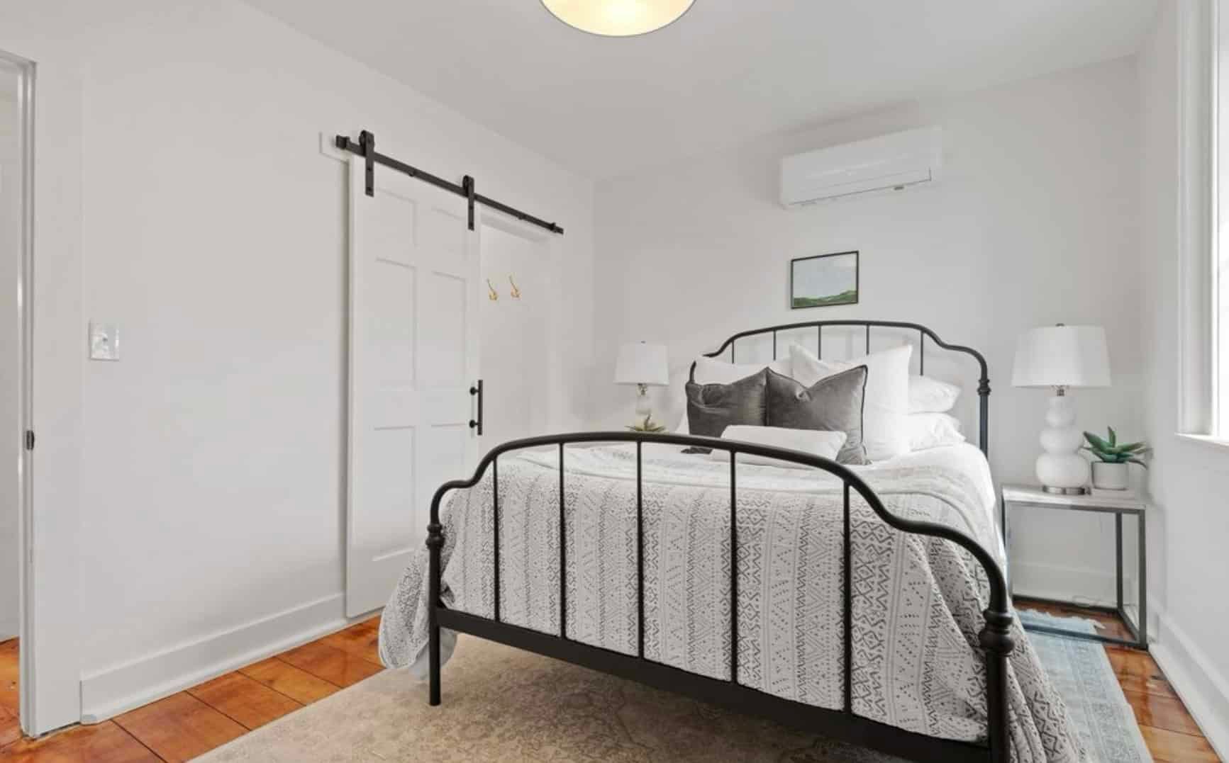 A bedroom with a bed , nightstand , lamps and a sliding barn door.