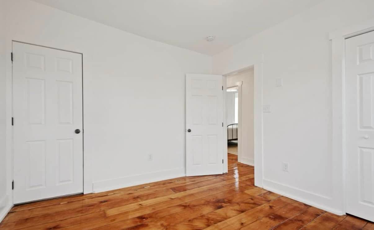 An empty bedroom with hardwood floors and white walls.