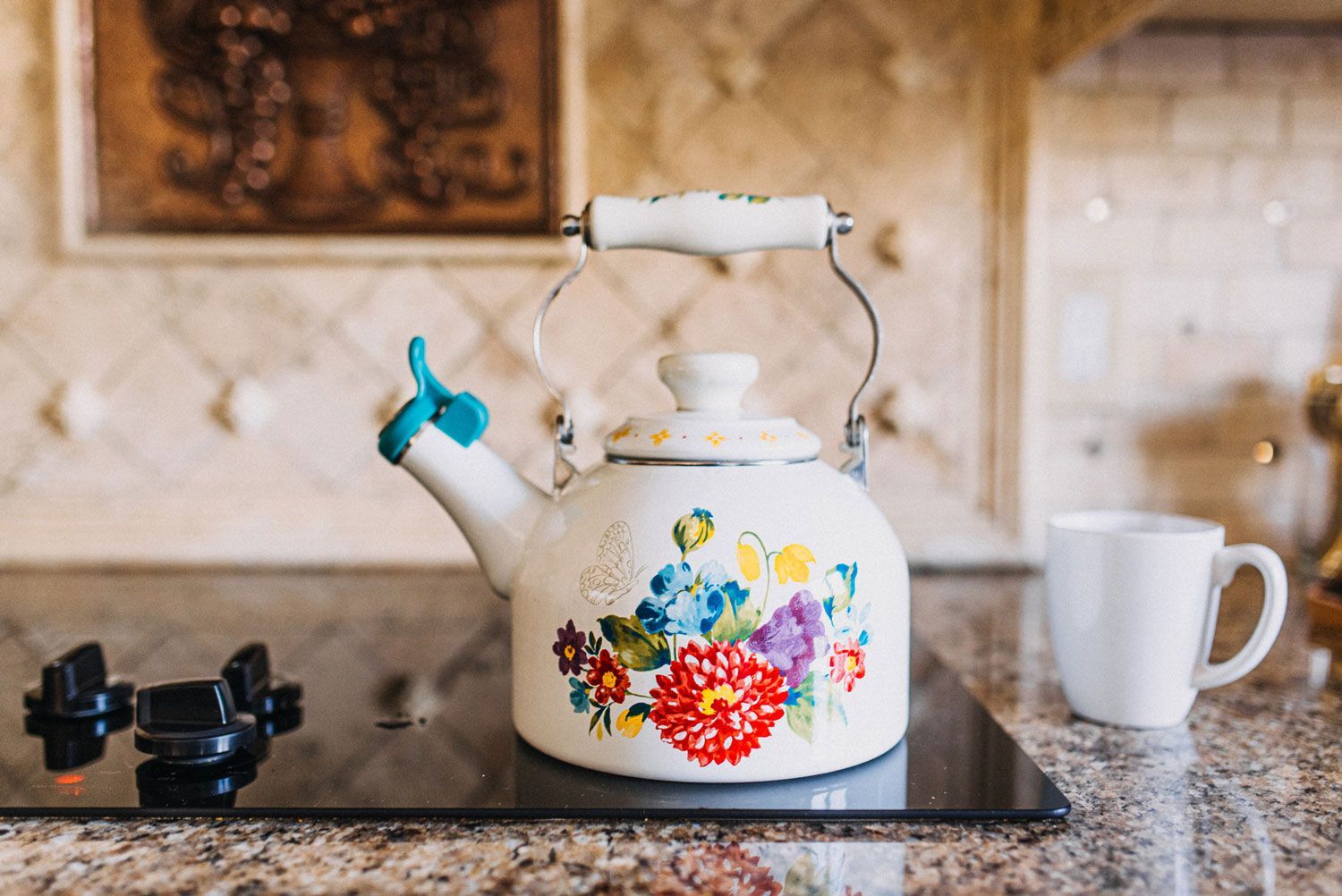 A tea kettle is sitting on top of a stove next to a cup of coffee.