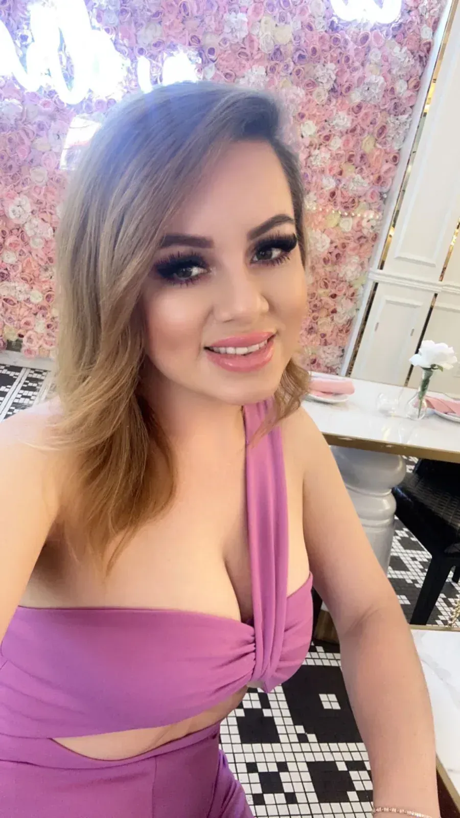 Woman in purple dress, smiling, with floral backdrop.