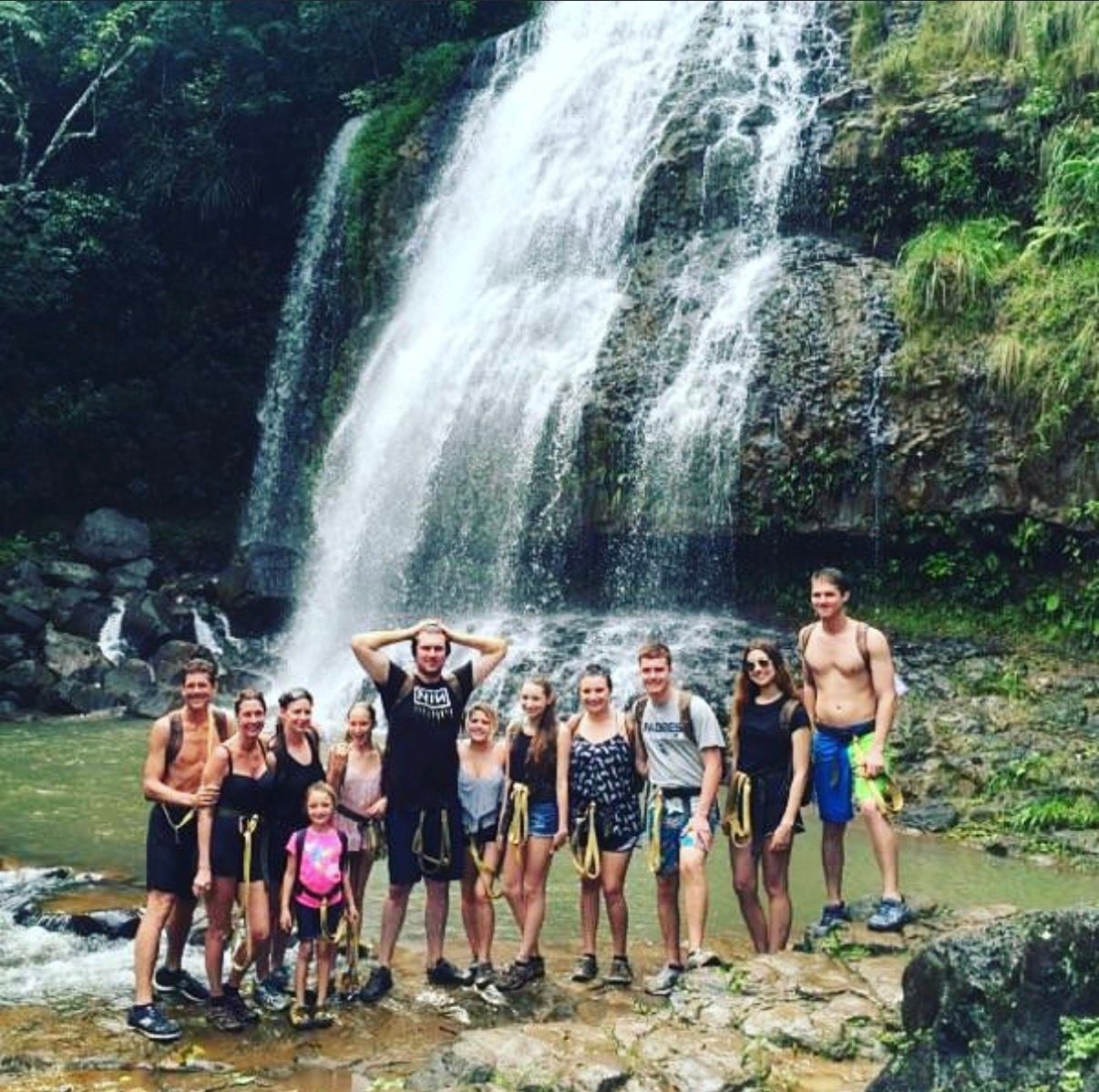 Group posing at the base of a waterfall in a lush Hawaii forest.