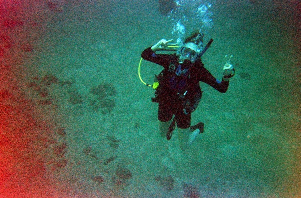 Scuba diver underwater above a sandy seafloor, with bubbles and green-blue water around them - Hawaii