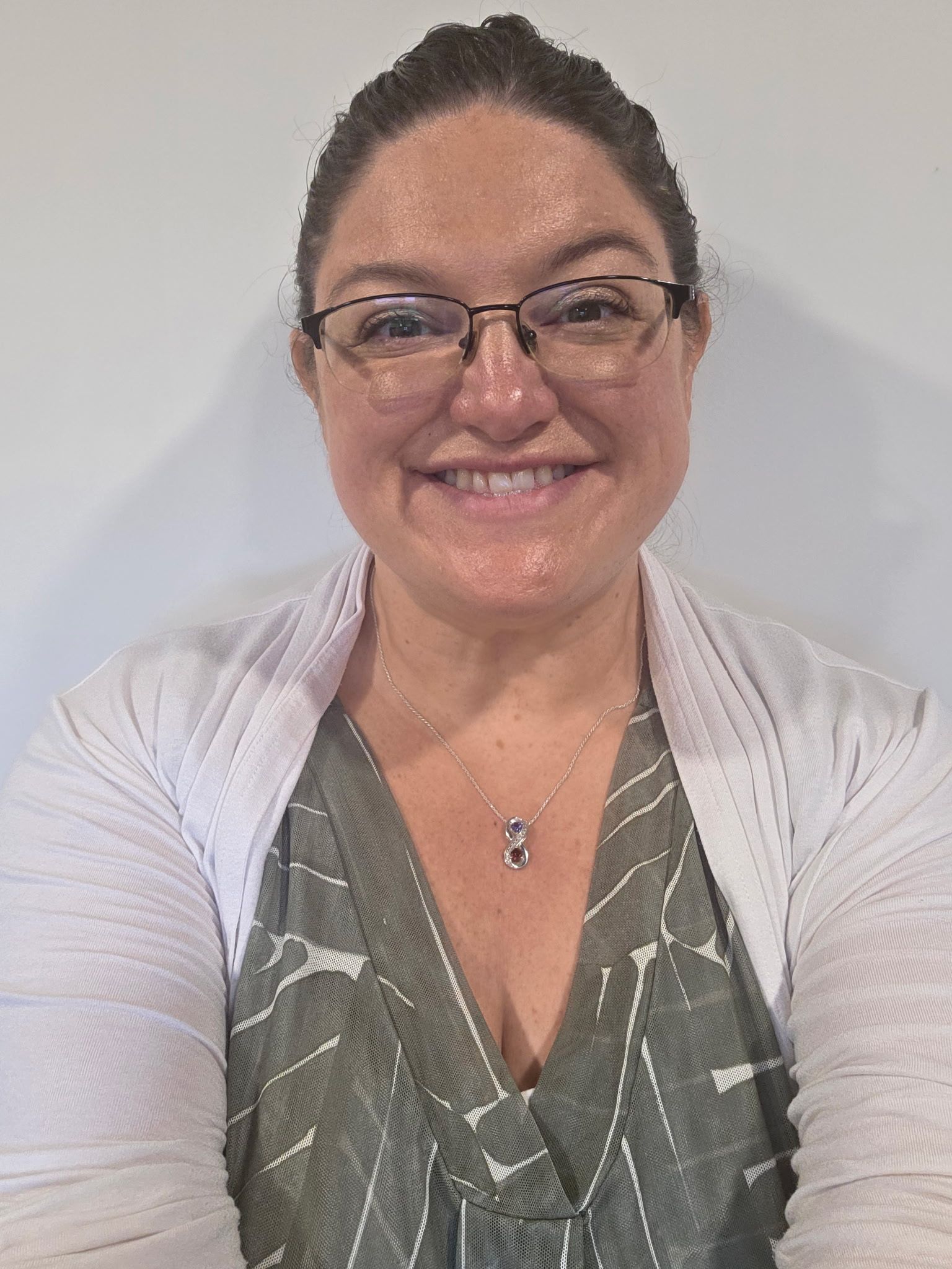 A smiling person with dark hair, wearing large gold hoop earrings against a neutral grey background.