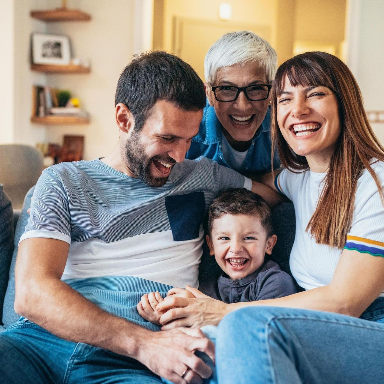 A smiling family of four sitting together on a couch at home, laughing and embracing.