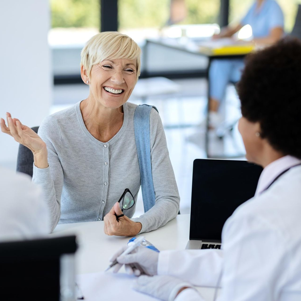 A professional in a lab coat consults with a smiling client at a desk in a bright office.