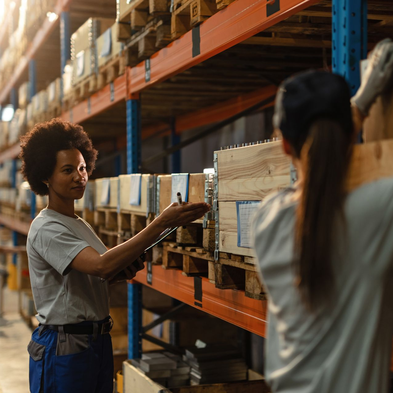 A forklift parked in the center of a narrow warehouse aisle flanked by tall metal shelves stacked with cardboard boxes.