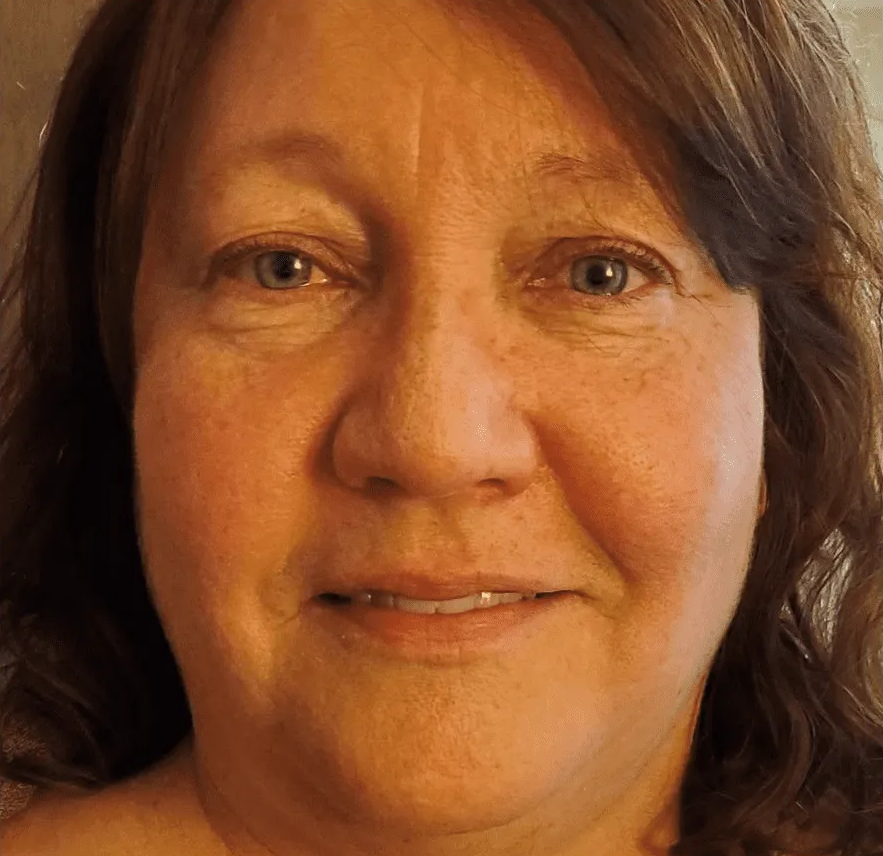 A close-up portrait of a person with brown hair and blue eyes, smiling gently at the camera.