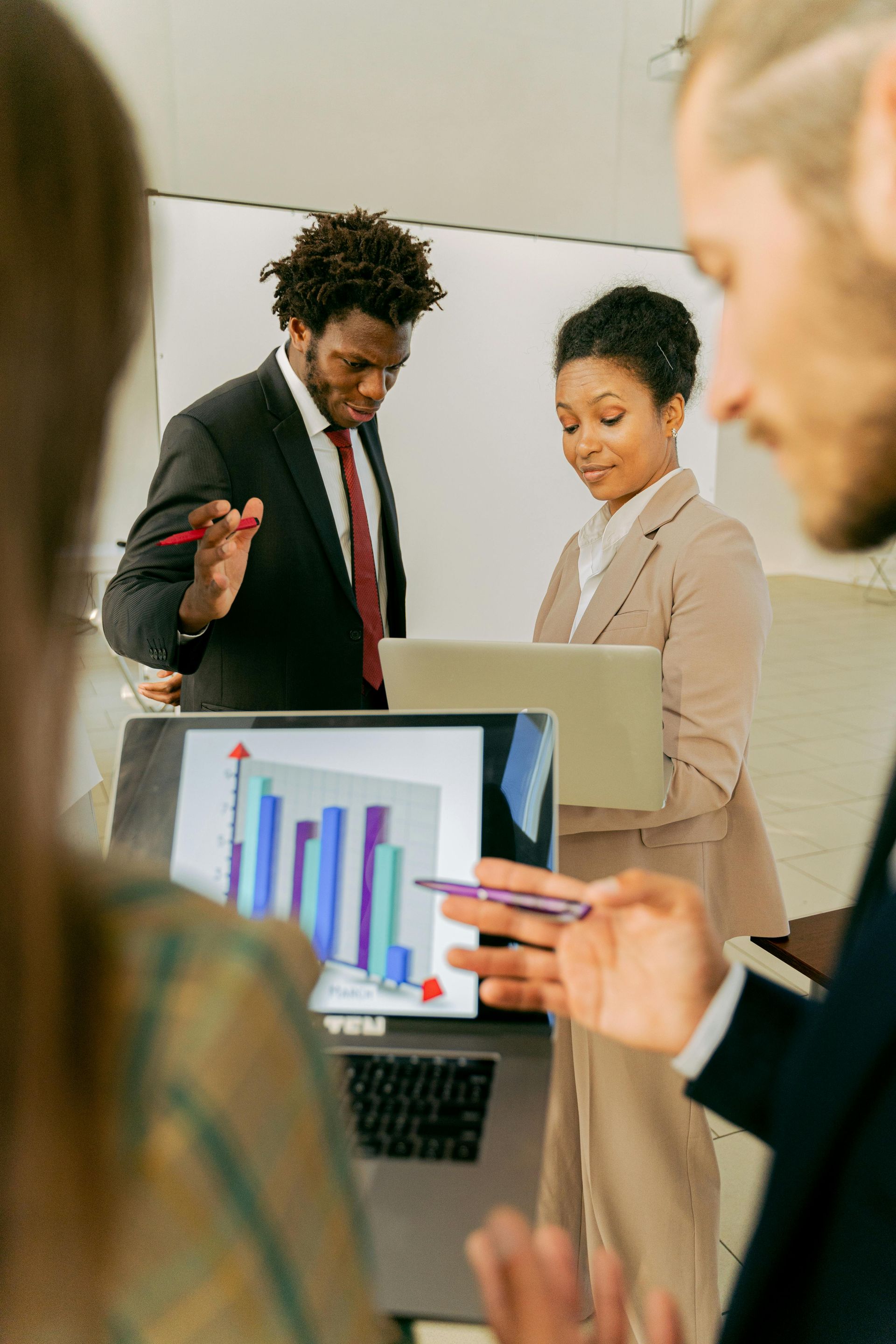 A diverse group of professionals in a bright office consult a laptop screen displaying a colorful bar graph.