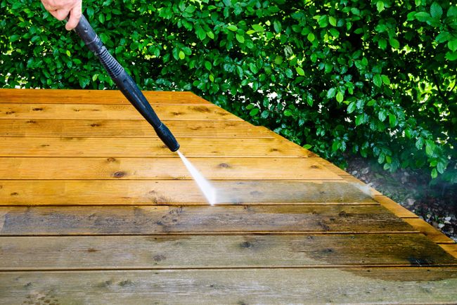a person is cleaning a wooden deck with a high pressure washer