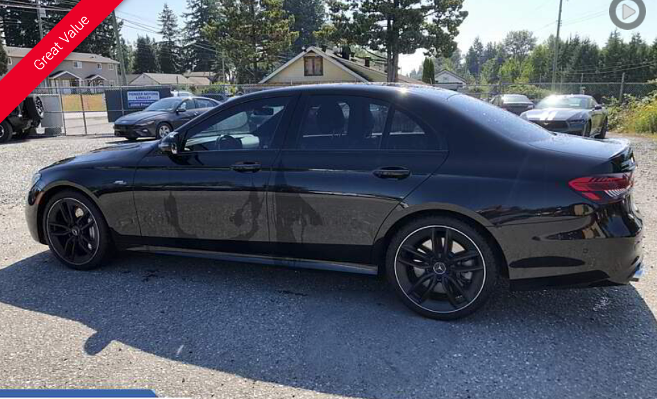 Black Mercedes sedan with black wheels parked on a gravel lot under a bright sky.