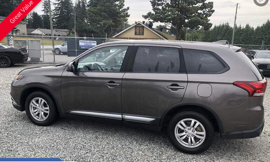 Gray Mitsubishi Outlander SUV parked on gravel at a car lot.