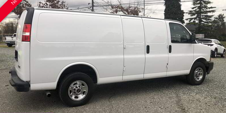 White cargo van parked on a gravel lot. It has side doors and black bumpers.