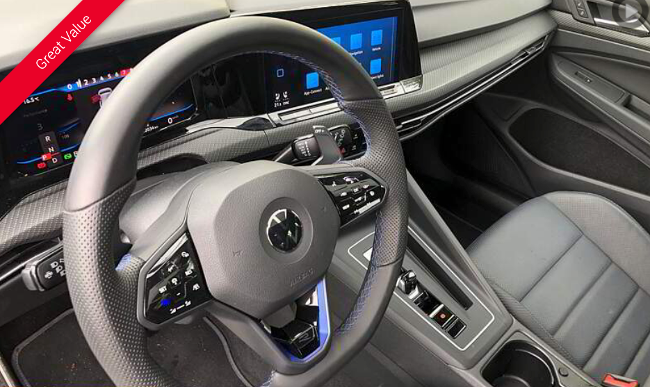Interior car shot, black steering wheel with controls and dashboard.