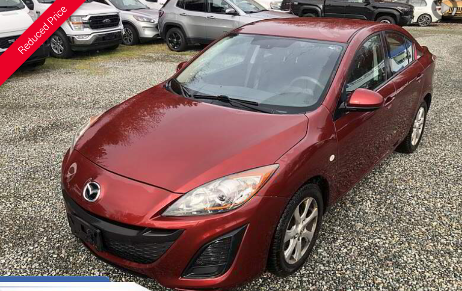 Red Mazda 3 sedan parked outside on gravel.