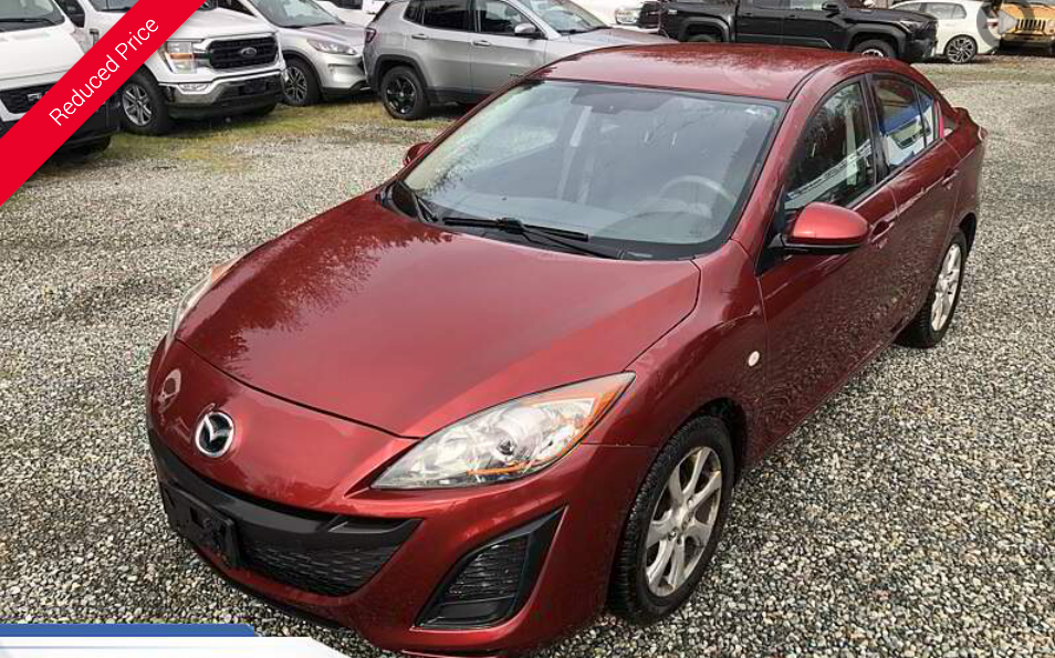 Red Mazda 3 sedan on a gravel lot.