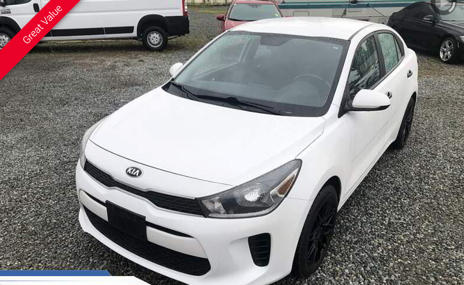 White Kia Rio sedan parked on gravel.